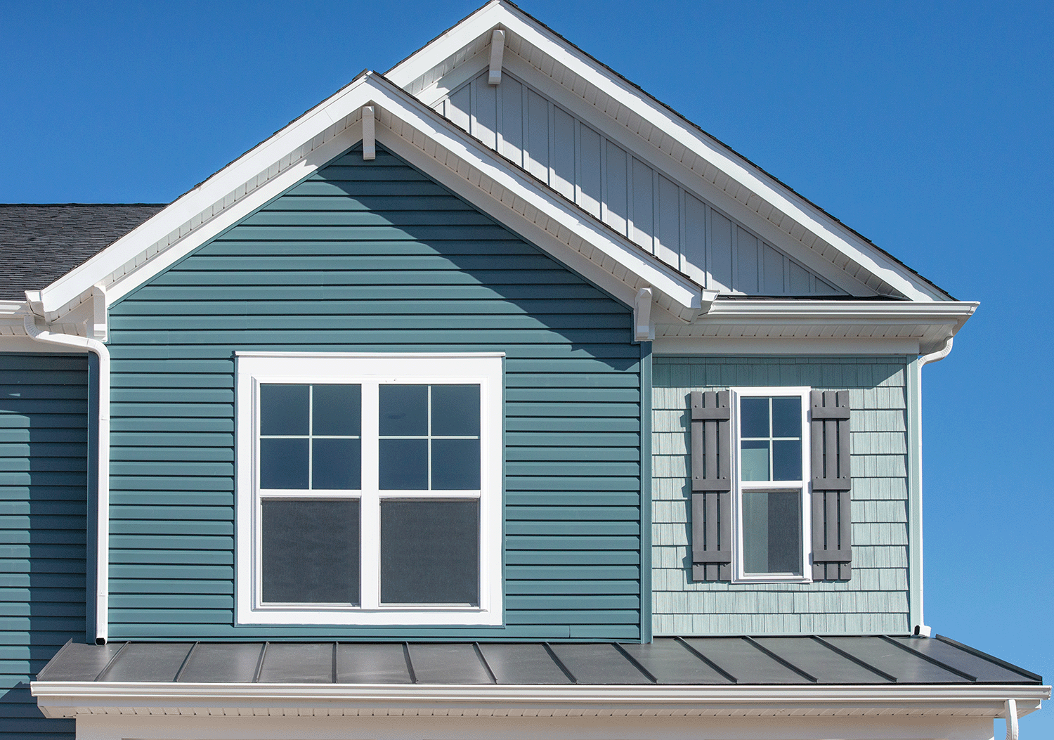 Crop of top section of the front of a house with three siding types. Horizontal traditional vinyl siding, rustic shake siding, and board and batten.