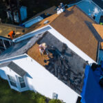 White house with roofers tearing off gray roofing shingles
