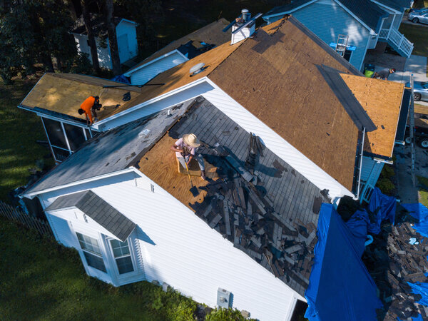 White house with roofers tearing off gray roofing shingles